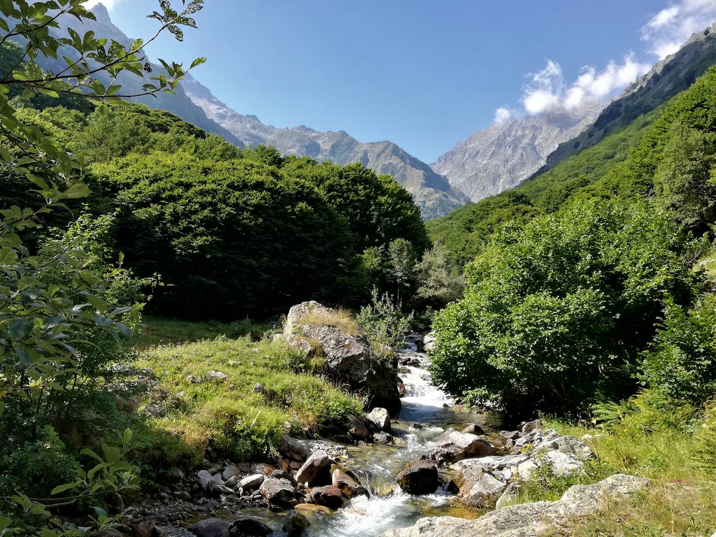 Eine kleine Schlucht mit Bergen im Hintergrund und ein wilder Fluss im Vordergrund - Wandern und Nachhaltigkeit