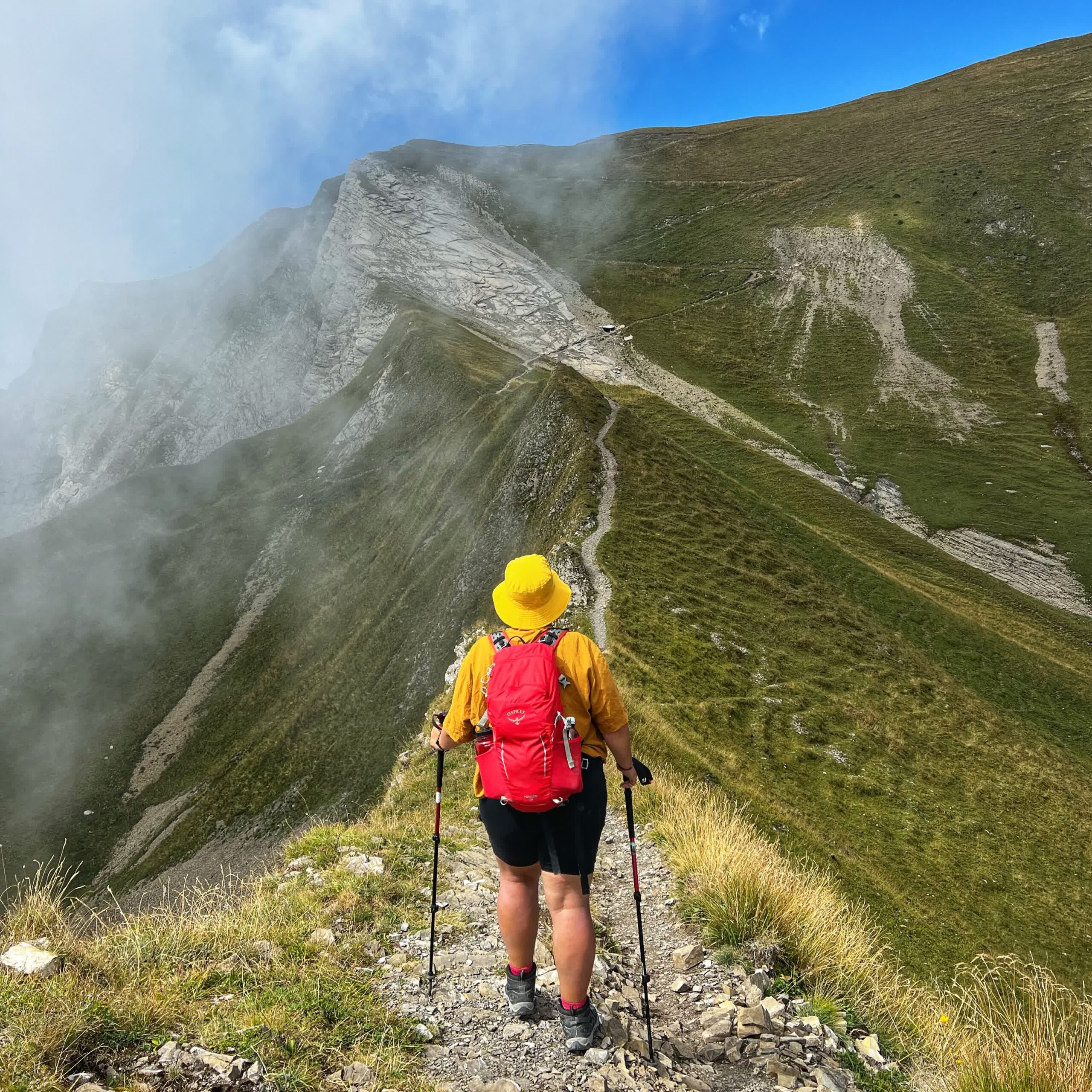 Frau mit rotem Rucksack geht auf einem Berggrat auf dem Tell-Trail in der Schweiz