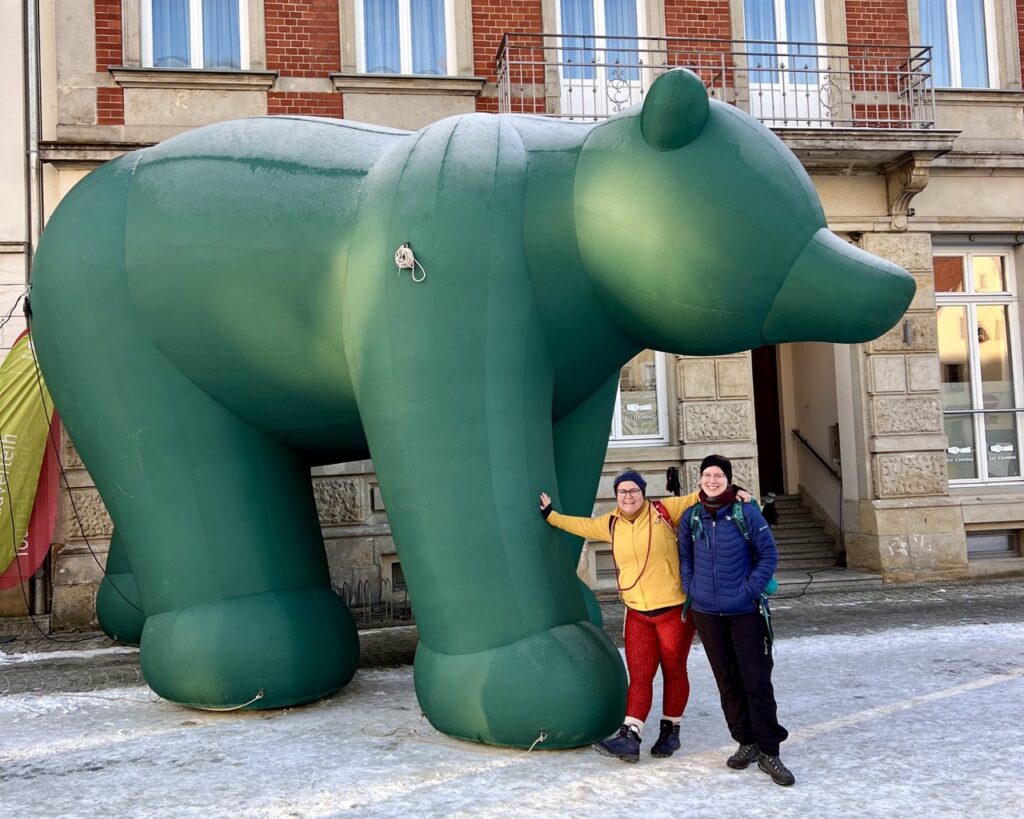 Ein großer grüner Aufblasbär vor dem zwei Frauen stehen - das Maskottchen der Globetrotter Winterwandertage